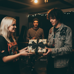 Young adults exchanging a gift wrapped in guitar-themed paper and black ribbon.