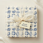 Square gift wrapped in nautical-themed paper with blue seashells and a cream ribbon.