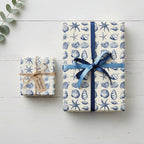 Elegant nautical gift wrap featuring blue seashell pattern and satin ribbon on a white wood background.