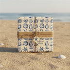 Elegant gift wrapped in blue seashell wrapping paper with rustic burlap ribbon, set on a sandy beach.