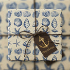 Square gift wrapped in nautical wrapping paper with seashells, starfish, and a brown twine bow.