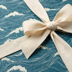 Ocean wave wrapping paper with a cream cotton ribbon bow, luxury coastal gift wrap by Wrapped Studios.