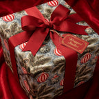 Luxury Christmas gift wrap with vintage pine and ornaments, tied with a red bow by Wrapped Studios.