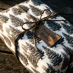 Rustic pine tree Christmas wrapping paper by Wrapped Studios, tied with a brown twine bow and tag.
