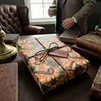 Vintage luxury gift wrap with pipe pattern by Wrapped Studios, tied with leather string in a library.