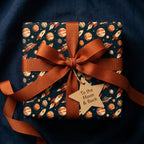 Outer space wrapping paper with planets and rockets, tied with a copper ribbon bow by Wrapped Studios.