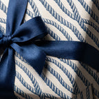 Nautical wrapping paper featuring a blue rope pattern and navy satin ribbon bow by Wrapped Studios.