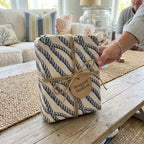 Hand holding a gift in nautical navy blue rope wrapping paper with twine bow, by Wrapped Studios.