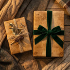 Cozy Christmas gift wrap: rustic kraft paper, green velvet bow, and eucalyptus with pinecones. Wrapped Studios.