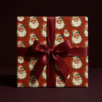 Retro Santa Christmas wrapping paper on a gift box with a burgundy satin bow by Wrapped Studios.
