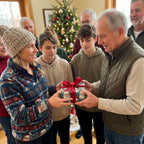 Family exchanging a Christmas gift wrapped in Santa-themed Christmas gift wrap with a red ribbon.