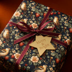 Elegant Christmas gift wrap featuring a bird, strawberry, and floral pattern with a burgundy ribbon and star tag.