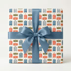 Travel wrapping paper with watercolor suitcases and a blue satin bow on a gift box by Wrapped Studios.