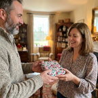Smiling couple exchanging a Christmas gift in vintage holiday wrapping paper by Wrapped Studios.