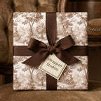 Vintage toile wrapping paper with a brown ribbon on a luxury gift box, by Wrapped Studios.