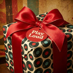 Retro vinyl record wrapping paper with a red satin bow and 'Play Loud' tag, by Wrapped Studios.