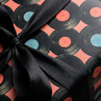 Retro vinyl record wrapping paper in coral with a black satin bow, music gift wrap by Wrapped Studios.