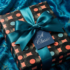 Vintage vinyl record wrapping paper with a teal satin bow and gift tag by Wrapped Studios.