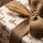 Rustic farmhouse wrapping paper with brown windmill pattern, burlap ribbon, and dried wheat by Wrapped Studios.