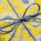 Yellow floral wrapping paper with a blue twine bow, elegant birthday gift wrap by Wrapped Studios.