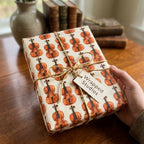 Hand holding a gift in vintage violin wrapping paper with a twine bow and a Wrapped Studios tag.