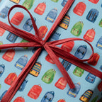 Back to school wrapping paper with a colorful backpack pattern and red raffia bow by Wrapped Studios.