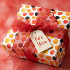 Wrapped Studios balloon birthday wrapping paper on a gift box with a red organza bow and For You tag.