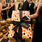 Festive balloon wrapping paper with black ribbon and Cheers tag at a party, by Wrapped Studios.
