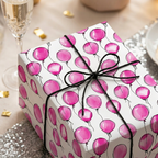 Gift wrapped in pink balloon pattern birthday wrapping paper and tied with black string.