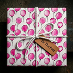 Square gift wrapped in pink balloon birthday wrapping paper, tied with white string, tag reads "To: The Best".