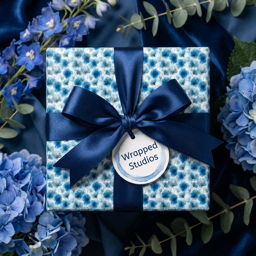 Elegant blue floral wrapping paper by Wrapped Studios on a gift box with a navy satin bow and hydrangeas.