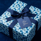 Luxury blue floral wrapping paper on a gift box with a navy bow and tag by Wrapped Studios.