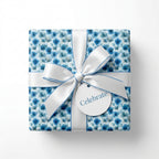 Blue floral wrapping paper with white ribbon and celebrate tag, elegant gift wrap by Wrapped Studios.