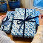 Hands tying navy ribbon on luxury blue floral wrapping paper by Wrapped Studios.