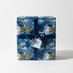 Square gift box wrapped in abstract blue pattern paper, tied with navy ribbon and tag.