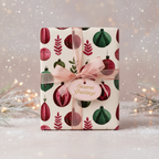 Christmas gift wrap with a festive ornament pattern, tied with a sheer pink ribbon and a "Seasons Greetings" tag on a snowy background.