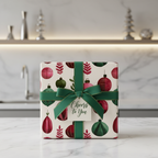 Luxury Christmas gift wrap with a festive ornament pattern in red and green, tied with a dark green ribbon and "Cheers to You" tag.