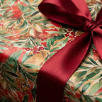 Festive watercolor Christmas wrapping paper featuring red berries, green foliage, and a dark red satin bow.