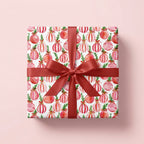 Pink watercolor ornament Christmas wrapping paper on a gift box with a red bow by Wrapped Studios.