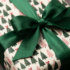 Luxury holiday gift wrap with a forest green satin bow and Christmas tree pattern by Wrapped Studios.