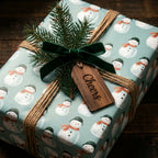 Rustic snowman Christmas wrapping paper with a green velvet bow and wooden tag by Wrapped Studios.