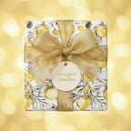 Square gift wrapped in Christmas wrapping paper with gold ornament design and gold ribbon.