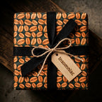 Coffee bean wrapping paper with a black ribbon and rustic tag by Wrapped Studios.