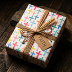 Christian cross wrapping paper with colorful watercolor pattern, rustic twine, and FAITH tag by Wrapped Studios.