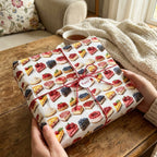 Hands holding a gift wrapped in dessert-themed wrapping paper with red twine and a tag that reads "Yum!".