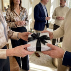 Hands exchanging a gift in elegant white floral wrapping paper with a black ribbon bow by Wrapped Studios.