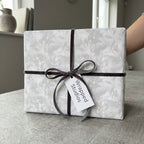 Elegant grey floral wrapping paper by Wrapped Studios on a gift box tied with a dark velvet bow.
