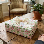 Elegant pink floral wrapping paper with a cream ribbon on a wooden table. Gift wrap by Wrapped Studios.