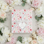 Elegant floral wrapping paper with lace ribbon and "Best Wishes" tag, surrounded by blush and white roses.