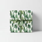Elegant Christmas gift wrap featuring watercolor pine tree pattern with green ribbon.